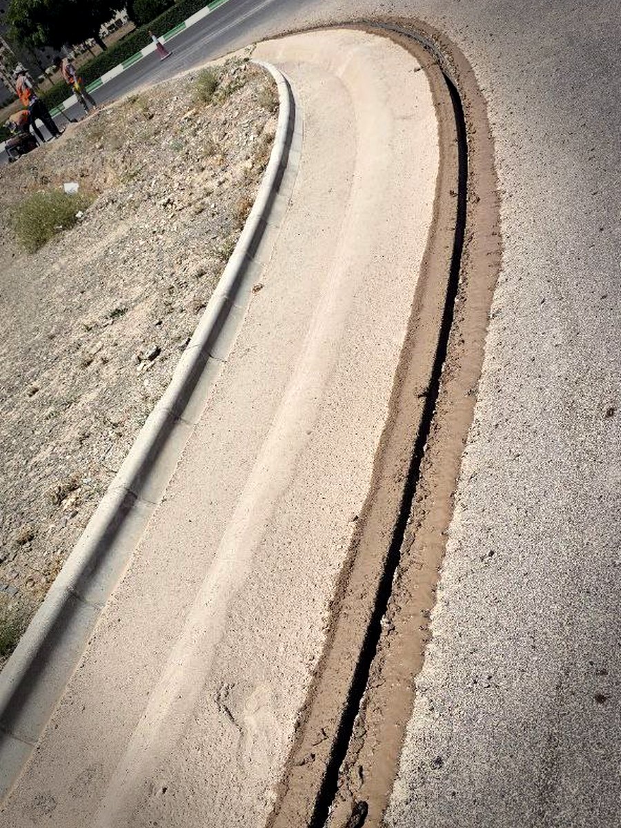 A continuous cut following the curve of the kerb; the asphalt and kerb stones around it are left intact.